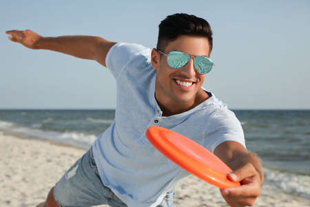 Happy man throwing flying disk at beach on sunny dayの写真素材