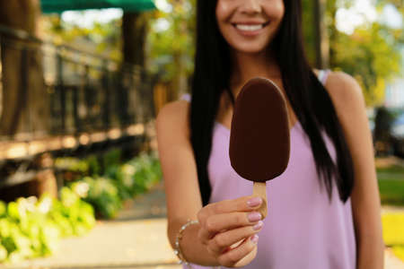 Young woman holding ice cream glazed in chocolate on city street, closeup. Space for textの写真素材
