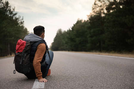 Man with backpack sitting on road near forest, back viewの写真素材