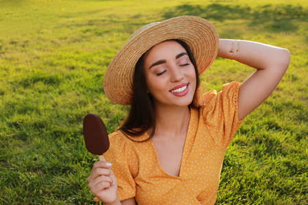 Beautiful young woman holding ice cream glazed in chocolate outdoorsの写真素材