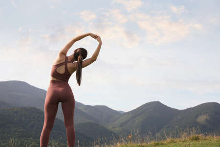 Woman doing morning exercise in mountains, back view. Space for text