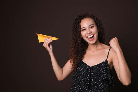 Beautiful African-American woman playing with paper plane on brown backgroundの写真素材
