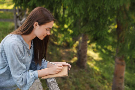 Beautiful young woman drawing with pencil in notepad near wooden fenceの写真素材
