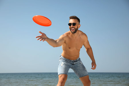 Happy man throwing flying disk at beach on sunny dayの写真素材