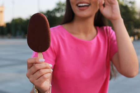 Young woman holding ice cream glazed in chocolate on city street, closeupの写真素材