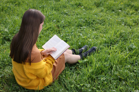 Young woman reading book on green grassの写真素材