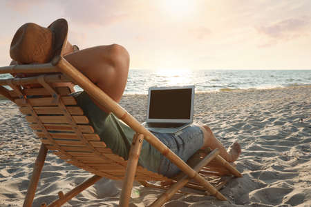 Man with laptop relaxing in deck chair on beachの写真素材