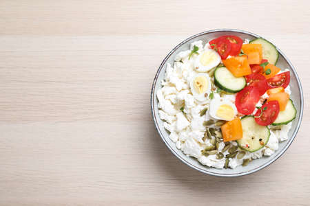 Fresh cottage cheese with vegetables, seeds and eggs in bowl on wooden table, top view. Space for textの写真素材