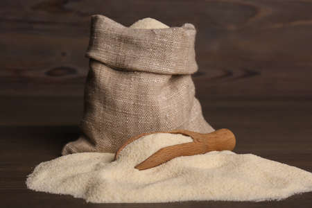Bag and scoop with uncooked organic semolina on wooden tableの写真素材
