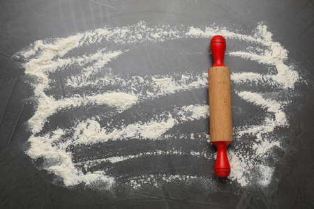Rolling pin and flour on black table, top view. Space for text