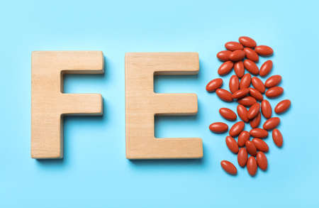 Wooden letters FE and pills on light blue background, flat lay. Anemia treatmentの写真素材