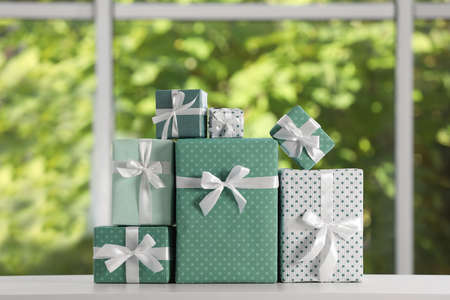 Many beautifully wrapped gift boxes on white table near windowの写真素材