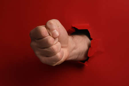 Man breaking through red paper with fist, closeupの写真素材