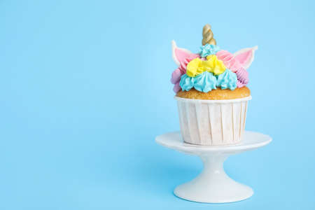 Dessert stand with cute sweet unicorn cupcake on light blue background. Space for textの写真素材
