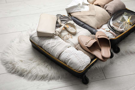 Open suitcase with folded clothes, shoes and accessories on floorの写真素材