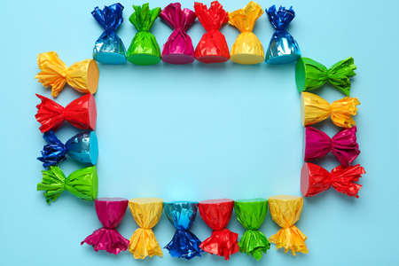 Frame of candies in colorful wrappers on light blue background, flat lay. Space for textの写真素材