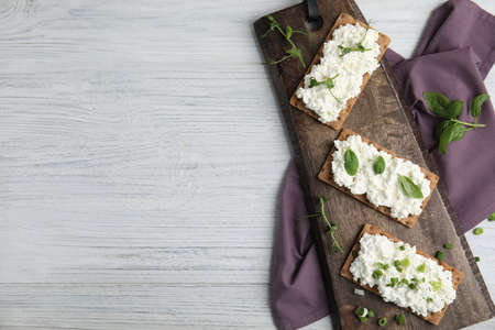 Crispy crackers with cottage cheese and different herbs on white wooden table, flat lay. Space for textの写真素材