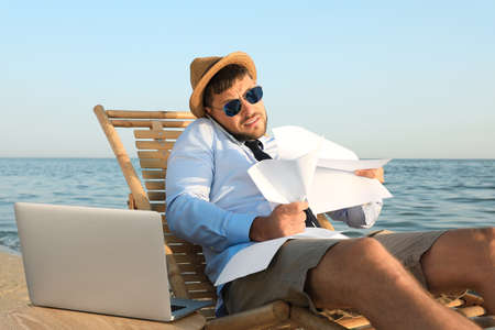 Busy man with papers talking by mobile phone on beach. Business tripの写真素材