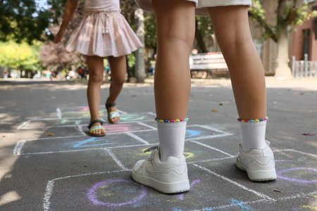 Little children playing hopscotch drawn with chalk on asphalt outdoors, closeupの写真素材