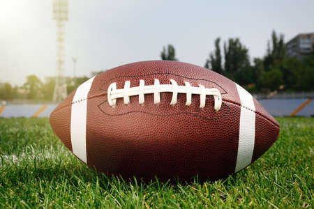 American football ball on green field grass in stadium