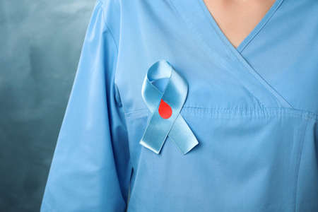 Doctor with light blue ribbon and paper blood drop on color background, closeup. World Diabetes Dayの写真素材