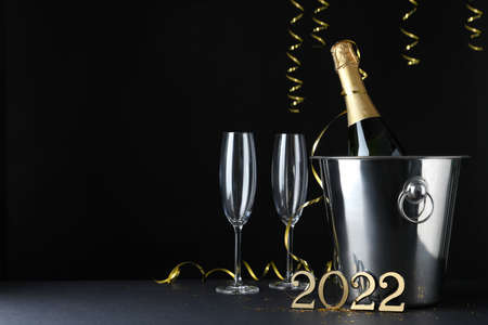 Happy New Year 2022! Bottle of sparkling wine in bucket and glasses on table against black background, space for textの写真素材