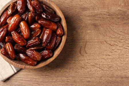 Tasty sweet dried dates in bowl on wooden table, top view. Space for textの写真素材