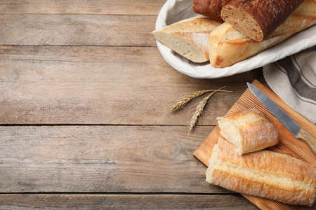 Different tasty baguettes, knife and spikelets on wooden table, flat lay. Space for text