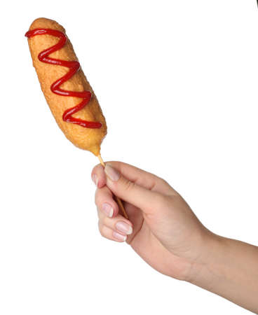 Woman holding delicious deep fried corn dog with ketchup on white background, closeupの写真素材