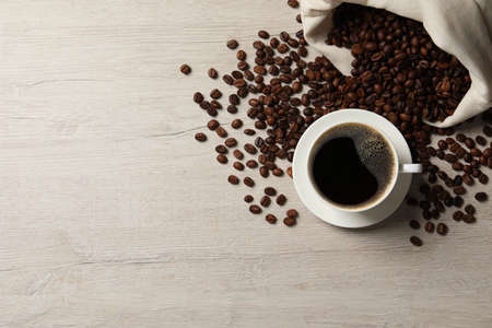 Cup of aromatic coffee and beans on light wooden table, flat lay. Space for text