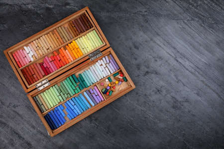 Set of colorful pastels in wooden box on gray stone table, top view with space for text. Drawing materialsの写真素材