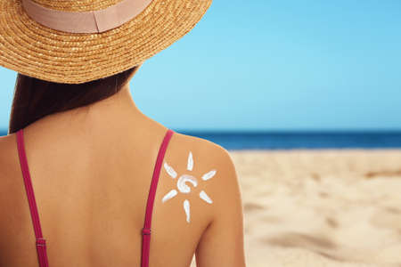 Young woman with sun protection cream on sandy beach, space for textの写真素材