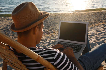 Man working with laptop in deck chair on beachの写真素材