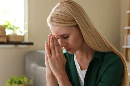 Religious young woman with clasped hands praying indoorsの写真素材