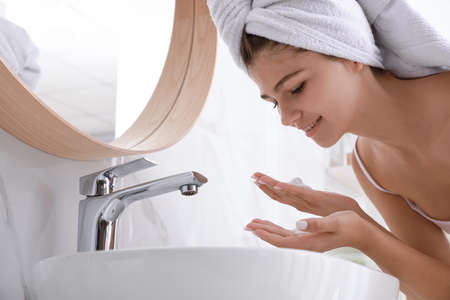Beautiful teenage girl washing face with cleansing foam in bathroom. Skin care cosmeticの写真素材