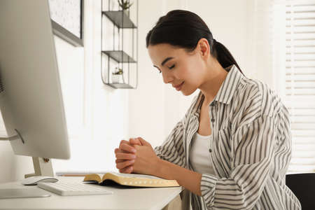 Beautiful young woman praying over Bible at deskの写真素材