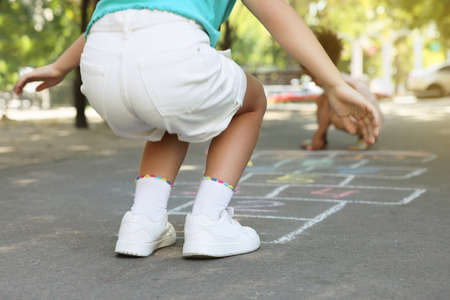 Little child playing hopscotch drawn with chalk on asphalt outdoors, closeup