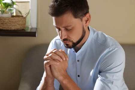 Religious man with clasped hands praying indoorsの写真素材