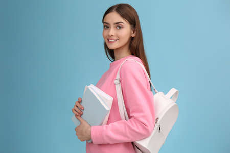 Teenage student with books and backpack on turquoise background