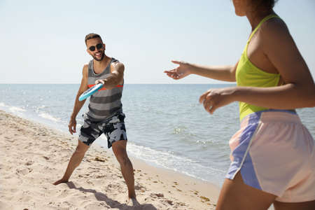 Couple playing with flying disk at beach on sunny dayの写真素材
