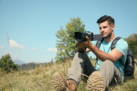 Professional photographer taking picture with modern camera in mountains. Space for text