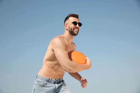 Happy man throwing flying disk against blue sky on sunny dayの写真素材