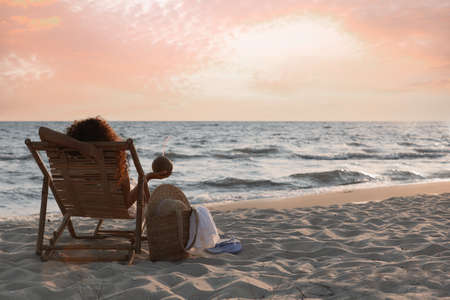 Woman with cocktail resting in wooden sunbed on tropical beach at sunsetの写真素材