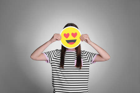 Woman covering face with heart eyes emoji on gray backgroundの写真素材