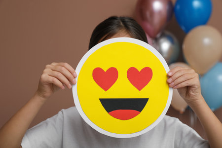 Little girl covering face with heart eyes emoji in decorated room
