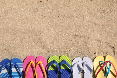 Many different flip flops on sand, flat lay. Space for textの写真素材