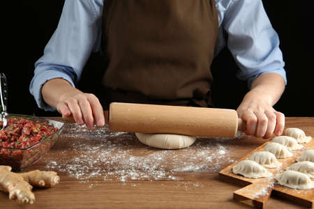 Woman rolling dough for gyoza at wooden table, closeup