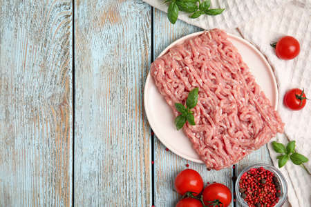 Raw chicken minced meat with basil, spices and tomatoes on light blue wooden table, flat lay. Space...