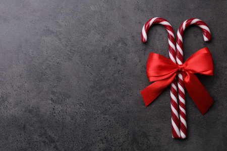 Sweet Christmas candy canes with red bow on gray background, top view. Space for text