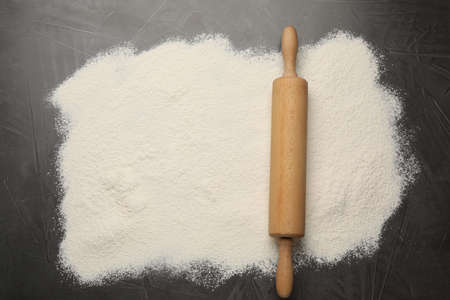 Rolling pin and flour on black table, top view. Space for text